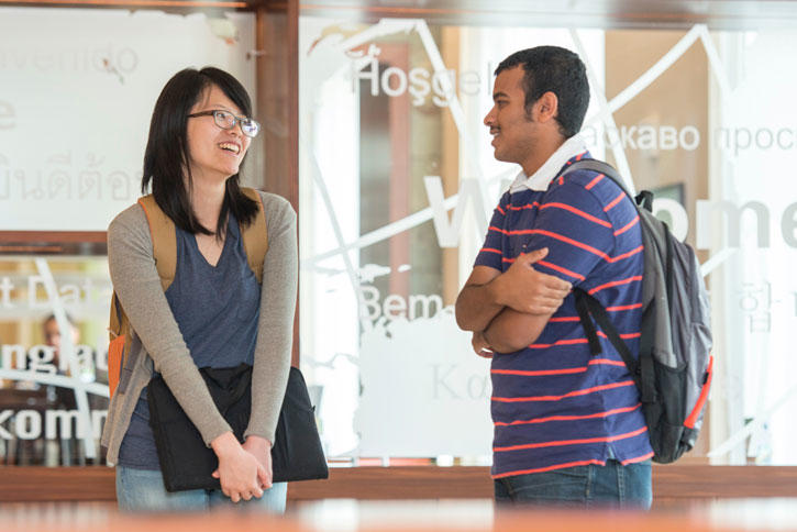 INTO Mason students chat in front of the glass welcome wall in the Global Center on the Fairfax Campus